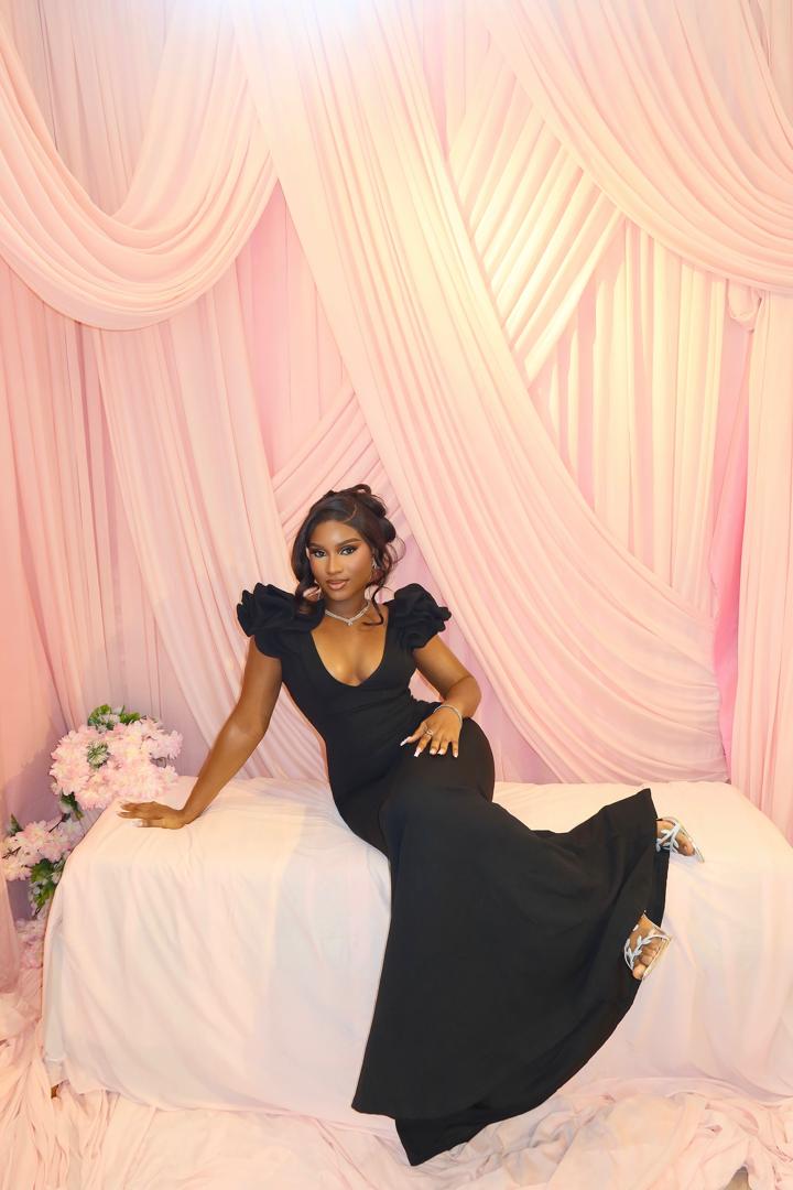 You in a black dress, sitting against soft pink drapes